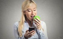 Blonde Consuming an Apple and making use of an App in her own Phone