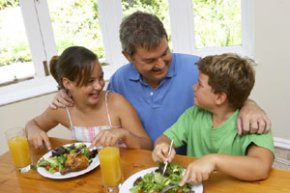 photo of 2 young ones and man eating salad and cooked chicken